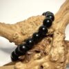 Bracelet en 8 mm en obsidienne noire posé sur morceau de bois