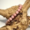Bracelet en 6 mm en rhodonite posé sur morceau de bois