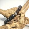 Bracelet homme en pierre d'oeil de tigre, d'oeil de faucon et d'oeil de taureau avec ornement en metal posé sur morceau de bois