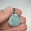 Pendentif format goutte en amazonite avec son attache en acier tenu par les doigts d'une main