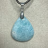 Pendentif format goutte en amazonite avec son attache en acier suspendu sur présentoir beige par cordon noir