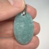 Pendentif format ovale en amazonite avec son attache en acier tenu par les doigts d'une main