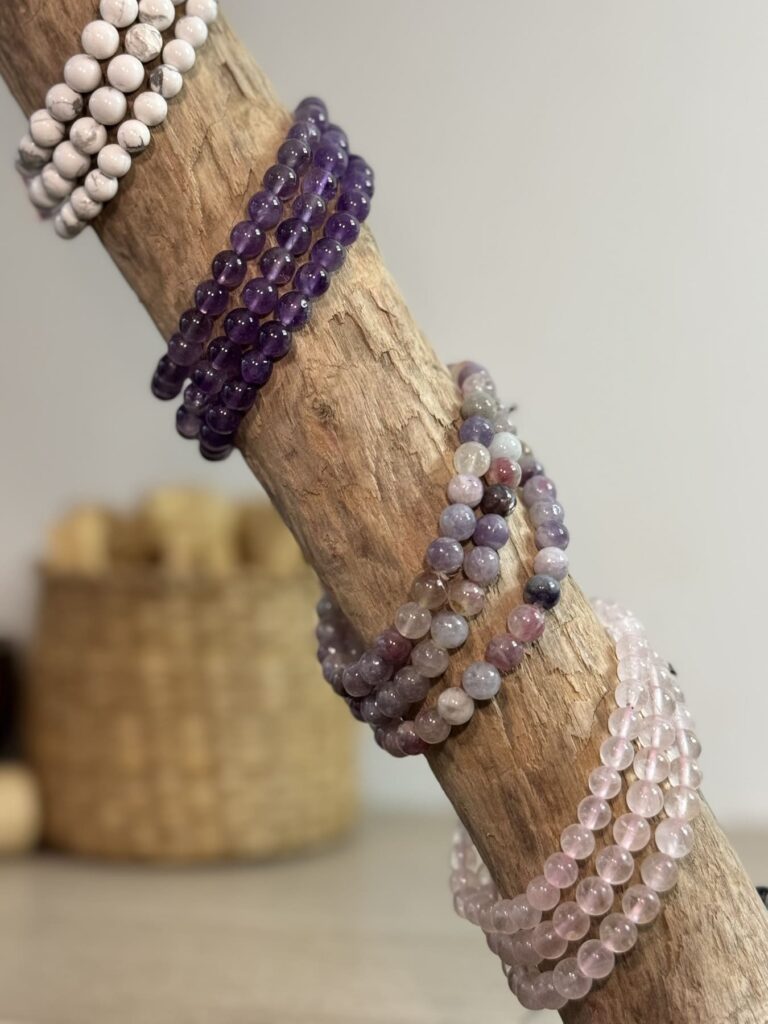 Bracelets en boules de quartz rose, puis de tourmaline multi, d'améthyste et d'howlite blanche posé sur morceau de bois