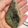Pendentif d'une coupe de 1 m d'une pierre en labradorite brute avec son attache en acier tenu dans une main