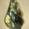 Pendentif d'une coupe de 1 m d'une pierre en labradorite brute avec son attache en acier suspendu par son cordon sur un présentoir beige