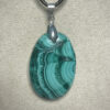 Pendentif format ovale en malachite avec son attache en acier suspendu sur présentoir beige par cordon noir
