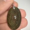 Pendentif en obsidienne Manta Huichol format ovale avec son attache en acier tenu par les doigts d'une main
