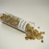 Tube à essai en verre renversé contenant de l'encens en grain doliman. On voit l'étiquette Oliban Encens collé sur le tube et des grains d'encens dépassant du tube.