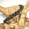 Bracelet en perle de lave 6 mm posé sur morceau de bois