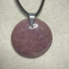 Pendentif format rond en rhodonite avec son attache en acier suspendu sur présentoir beige par cordon noir