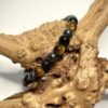 Bracelet en 6 mm. trio de protection de pierres d'oeil de tigre, d'obsidienne et d'hématite posé sur morceau de bois