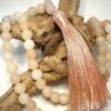Mala en Aventurine rose avec pompon d'ornement rose posé sur morceau de bois