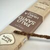 Partie de boite d'encens de palo Santo et vanille prise de biais avec une tige d'encens posé dessus