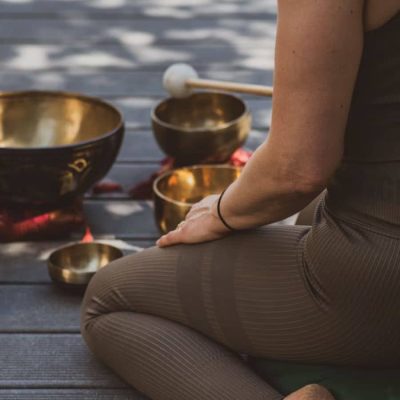 corps d'une femme de dos assis par terre les jambes repliés, des bols tibétains sur le sol